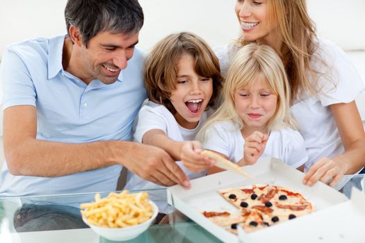 Excited children eating a pizza with their parents in the living-room