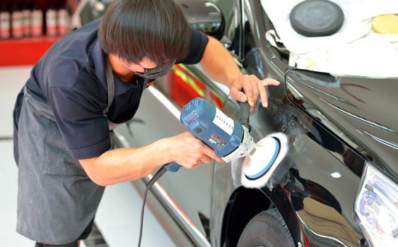 The man is polishing the black car with polish machine.