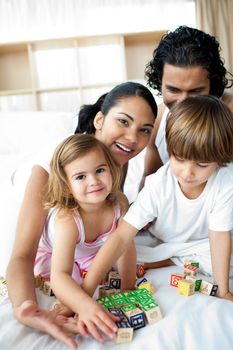 Portrait of a happy family playing with letter blocks on the bed