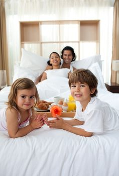 Siblings having breakfast with their parents lying on the bed