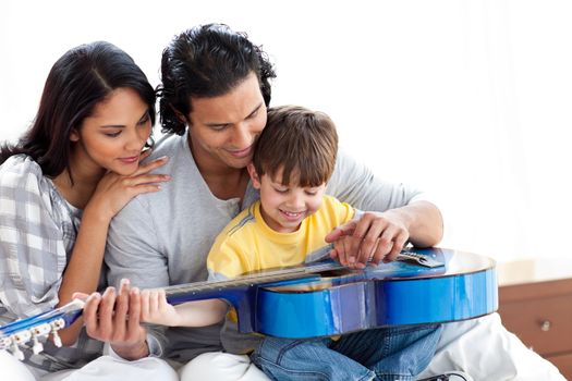 Happy little boy playing guitar with his parents at home