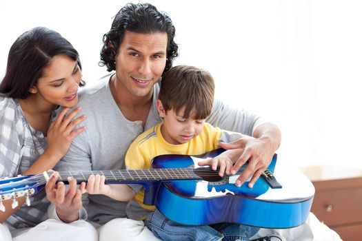 Cute little boy playing guitar with his parents at home