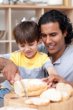 Attractive father helping his son cut some bread in the kitchen