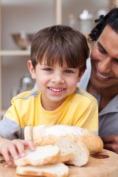 Smiling child eating bread with his father in the kitchen