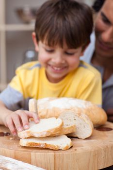 Adorable little boy eating bread with his father in the kitchen