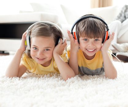 Smiling siblings listening music with headphones lying on the floor