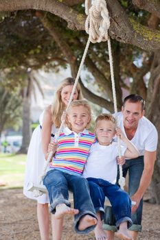 Happy parents pushing their children on a swing in a park