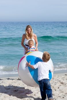 Caring mother and her children playing with a ball at the beach