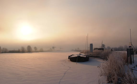 Sunrise in winter over a frozen canal and windmills at the famous dutch UNESCO site Kinderdijk, Holland.