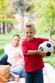 Little boy holding a soccer ball with his family in the backgroud