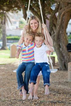 Smiling mother and her children swinging in a park