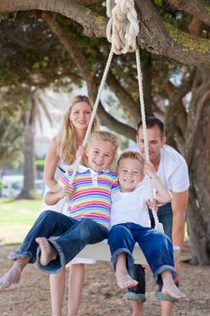 Joyful parents pushing their children on a swing in a park
