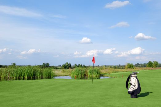 Golf field with red flag and white golf bag