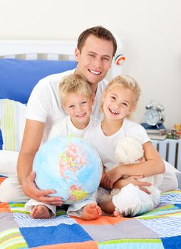 Cheerful father and his children holding a terretrial globe sitting on a bed