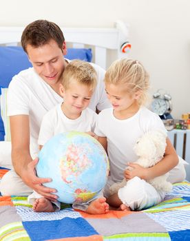 Jolly father and his children holding a terretrial globe sitting on a bed