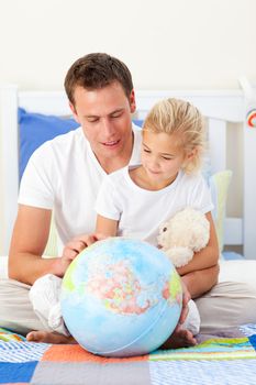 Attentive father and his daughter looking at a terretrial globe sitting on a bed