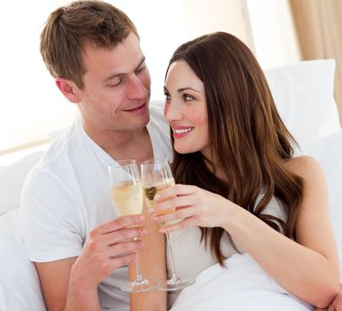 Romantic couple drinking champagne lying in bed at home