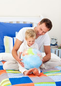 Laughing father and his son looking at a terrestrial globe sitting on bed