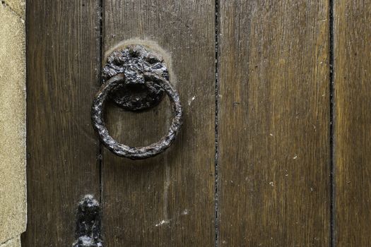 Old cast iron doorknocker on a wooden door in the form of an ornate circle to bang on the wooden surface to gain entry