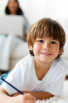 Smiling little boy drawing lying on the floor in the living-room