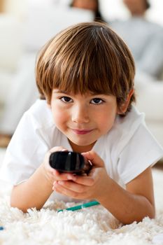 Smiling little boy holding a remote lying on the floor in the living-room