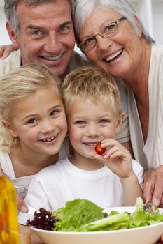 Happy grandparents eating a salad with grandchildren in the kitchen