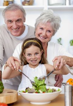 Smiling grandparents eating a salad with granddaughter in the kitchen