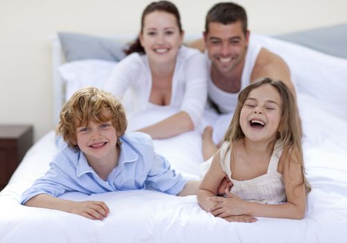Happy brother and sister having fun in bed with their parents
