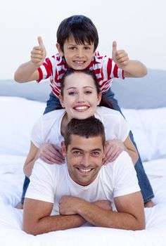 Happy parents and son playing in bed with thumbs up