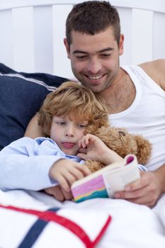 Little boy reading with his father a book in bed