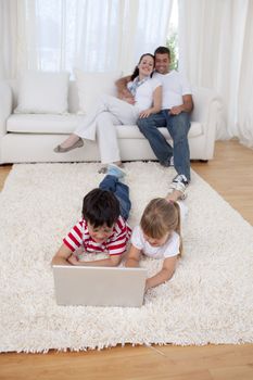 Brother and sister using a laptop on floor in living-room with their parents on sofa