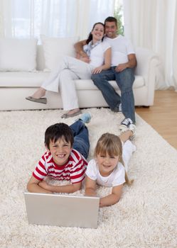 Children using a laptop on floor in living-room with their parents on sofa