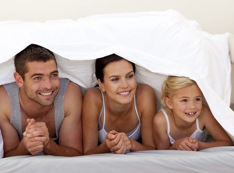Parents and daughter under the sheets in bedroom