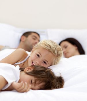 Little girl smiling on bed wile her parents and brother sleep
