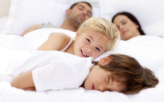 Smiling daughter relaxing with her brother and parents sleeping in bed