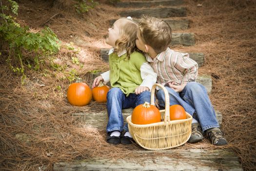Adorable Brother and Sister Children Sitting on Wood Steps with Pumpkins Whispering Secrets or Trying to Kiss Cheek.