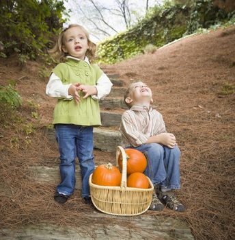 Adorable Brother and Sister Children Sitting on Wood Steps with Basket of Pumpkins Singing Songs Outside.