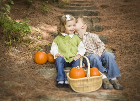 Adorable Brother and Sister Children Sitting on Wood Steps with Pumpkins Whispering Secrets or Kissing Cheek.