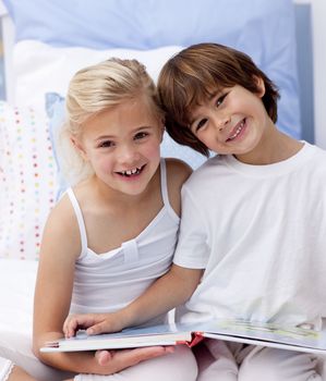 Happy little brother and sister reading a book in bedroom