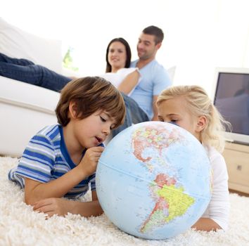 Children playing with a terrestrial globe in living-room with their parents on sofa