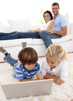 Children using a laptop on floor and parents lying on sofa