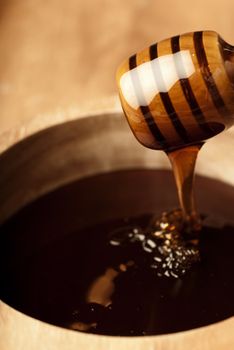 Dense honey in a wooden bowl dripping from a dripper