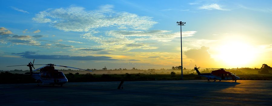 silhouette of helicopters on the apron with sunrise background