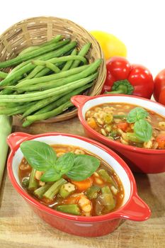 Minestrone with tomatoes, peppers, carrots, potatoes and basil on a bright background