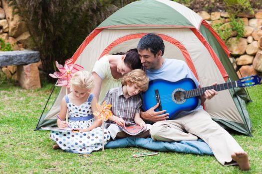 Happy parents and children playing a guitar in a tent