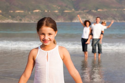 Cute girl on a beach with her parents and her brother in background