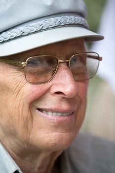 Senior man is smiling at camera with his classic gray hat and golden color glasses.
