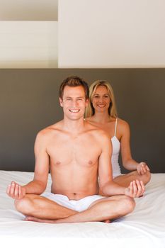Smiling young couple doing yoga on bed together