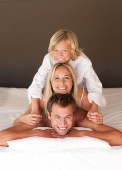 Portrait of happy parents and children having fun in bed and smiling at the camera 