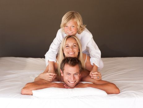Adorable little boy and his parents having fun lying on the bed at home